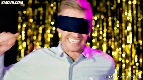 Blindfolded blonde man smiling excitedly pointing finger gun in shiny party background