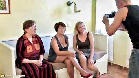 Young man films three mature women with big tits sitting on couch in tight clothes