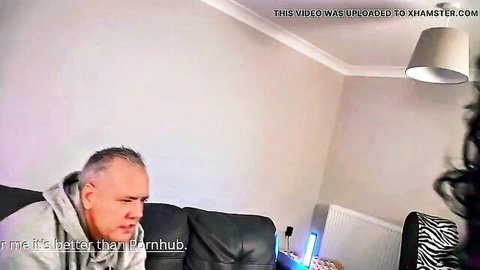 Mature grey-haired man in hoodie sits on black leather couch in British living room amateur video