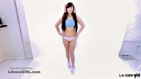 Cute young Asian girl with pigtails in blue sports top and pink shorts posing in studio