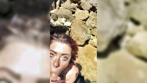 Blurry close-up of redhead woman with green eyes at rocky beach, voyeur found