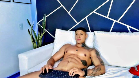 Muscular tattooed Latino Diagostone nude on couch, laptop on lap in gay dom scene