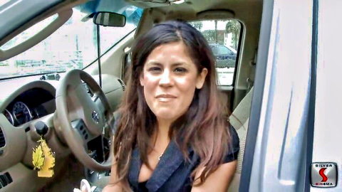 Brunette Latina MILF smiling with deep cleavage in SUV driver's seat