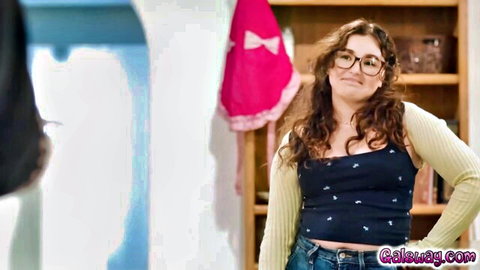 Leana Lovings in black tank top and jeans, curly hair and glasses, seductive expression