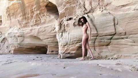 Slender dark-haired teen posing nude by rocks, stretching to show pussy