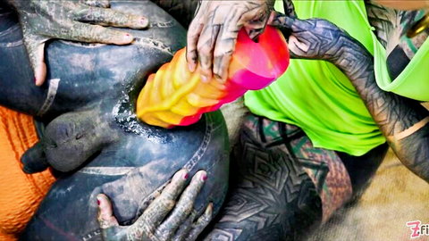 Tattooed hands shoving huge ridged yellow-pink dildo deep into stretched black-painted anus for extreme anal play