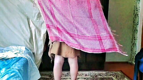 Cute sissy in short brown dress lifting pink checkered blanket, back view