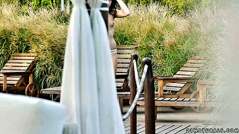 Skinny nude brunette teen with small tits and ass poses topless outdoors by poolside lounge chairs