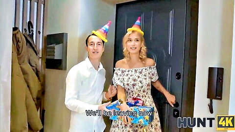 Smiling blonde in floral off-shoulder dress and party hat with young man at door, Hunt4K scene