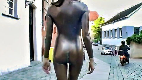 Woman walking in shiny black latex catsuit on urban street, emphasizing curves