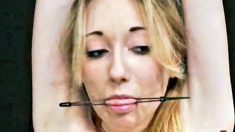 Skinny blonde restrained with arms raised and bit gag in mouth, BDSM bondage