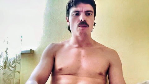 Muscular shirtless guy with mustache smirks bare-chested showing toned pecs on webcam