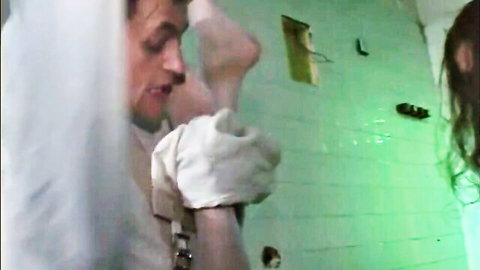 Madhouse nurse in white veil and gloves lifts patient's bare leg