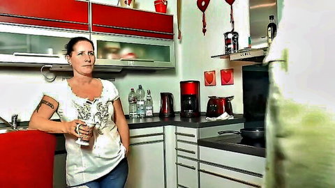Mature German woman in white top and jeans posing in kitchen