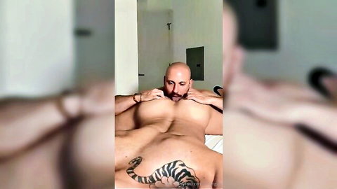 Muscular bald man with beard lying shirtless, showcasing lower body tattoo