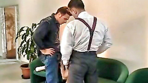 Two suited men in intimate standing pose, one gripping the other's hips