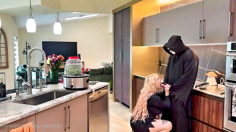 Blonde in black dress kneels before cloaked Grim Reaper in intimate pose