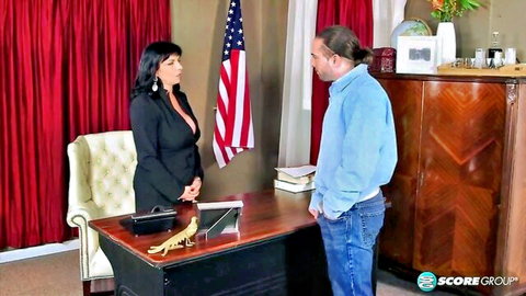 Brunette female politician in blazer at office desk with standing man, political anal tease