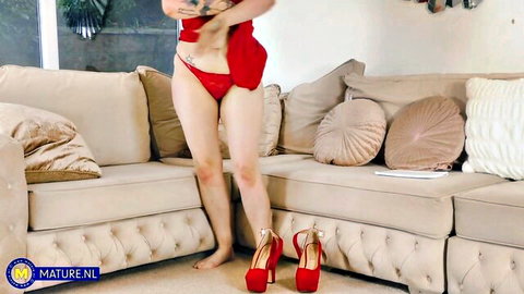 Tattooed brunette lifts red dress exposing shaved pussy in red thong and high heels