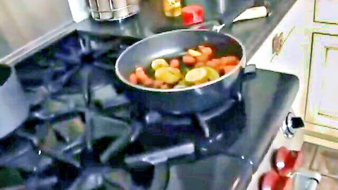 Close-up of sizzling sliced sausages and colorful vegetables frying in a pan on kitchen stove