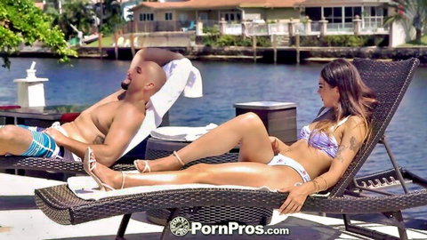 Sofie Reyez in purple bikini lounging poolside with muscular man, teasing pose