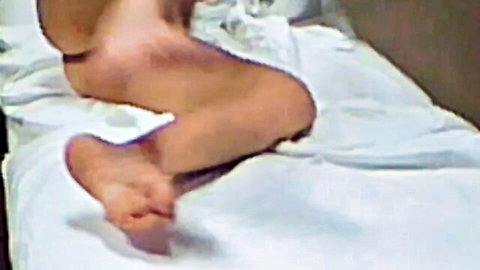 Blonde woman spreads legs on bed during lunch break, bare feet visible