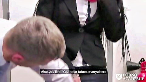 Tattooed woman in suit stands over kneeling man in teasing scene