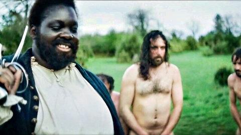 Grinning ebony pirate holds sword before three naked hairy white men exposing cocks outdoors