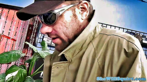 Rugged man in cap sunglasses and trench coat near plants and beaded curtain