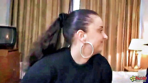 Chubby MILF with dark ponytail and hoop earrings smiling seductively in black top