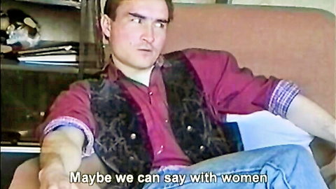 Gay man in red shirt and black vest sits on couch saying 'maybe we can say with women'