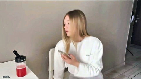 Sensual blonde Russian teen in white hoodie holding phone, teasing expression