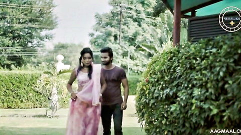 Seductive Indian woman in pink saree walks with man in outdoor garden