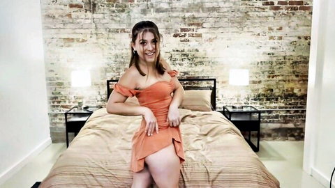 Curvy brunette in orange off-shoulder dress posing seductively
