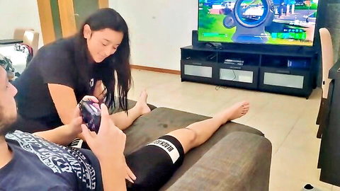 Asian gamer girl in black lingerie teases boyfriend's bulge with hand on thigh while he plays Nintendo Switch on couch