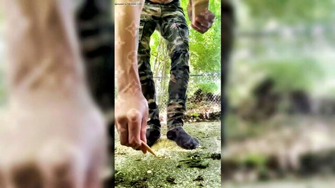 Woman in camo pants crushing giant cracker with black boots, tattooed arms