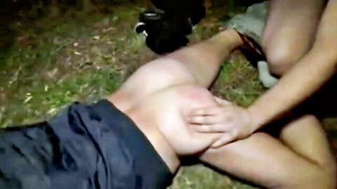 Woman squeezes naked man's pale ass cheek outdoors on grass in hot threesome