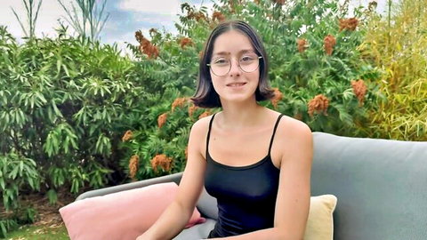 Penelope, 19, in black tank top and glasses, smiling solo outdoor tease