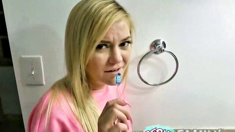 Blonde woman in pink top brushing teeth with pink toothbrush in bathroom