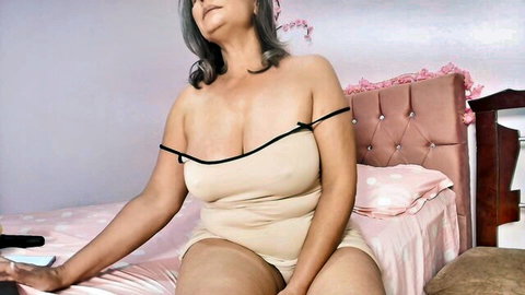 Busty mature MILF in sheer lingerie showing huge tits cleavage on pink bed