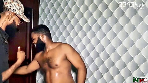 Muscular shirtless ebony hunk with beard poses sweaty as another black guy in hat flips middle finger