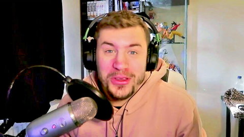 Man in pink hoodie with headset speaking into microphone in gaming stream setup