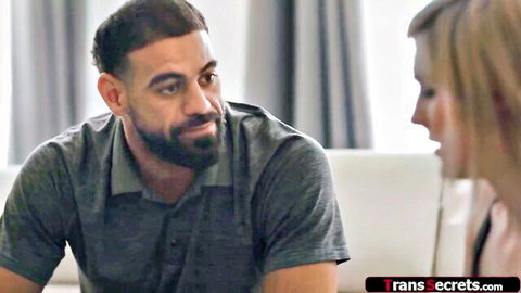 Blonde trans babe intimately facing bearded hunk on couch in teasing encounter