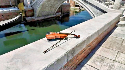 Orange violin resting on stone wall overlooking Venice canal with gondola and bridge