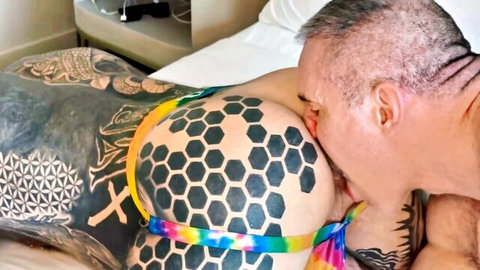 Tattooed couple in bed, man kissing woman's large inked breasts during intimate rimfest