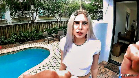 Blonde woman in white tank top outdoors by pool, hand near her mouth in teasing POV scene