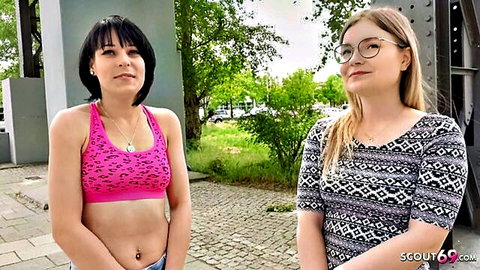 Brunette in skimpy pink leopard bra showing midriff poses with blonde glasses girl outdoors on street