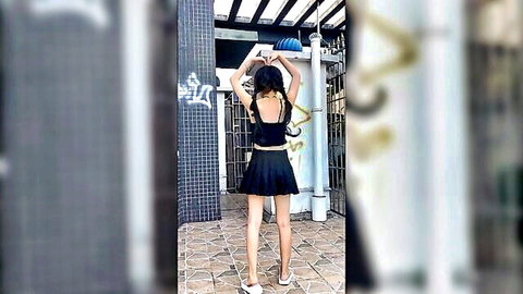 Asian teen in short black skirt and crop top posing outdoors from behind