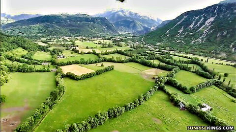 Aerial view of lush green valley with fields, river, and snowy mountains