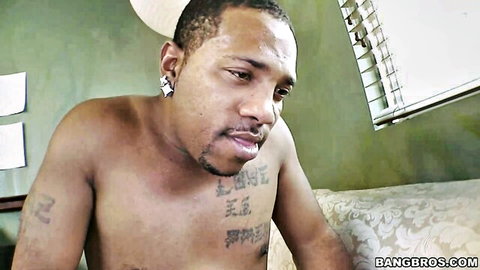 Shirtless tattooed black man with goatee smirking on couch in BangBros video